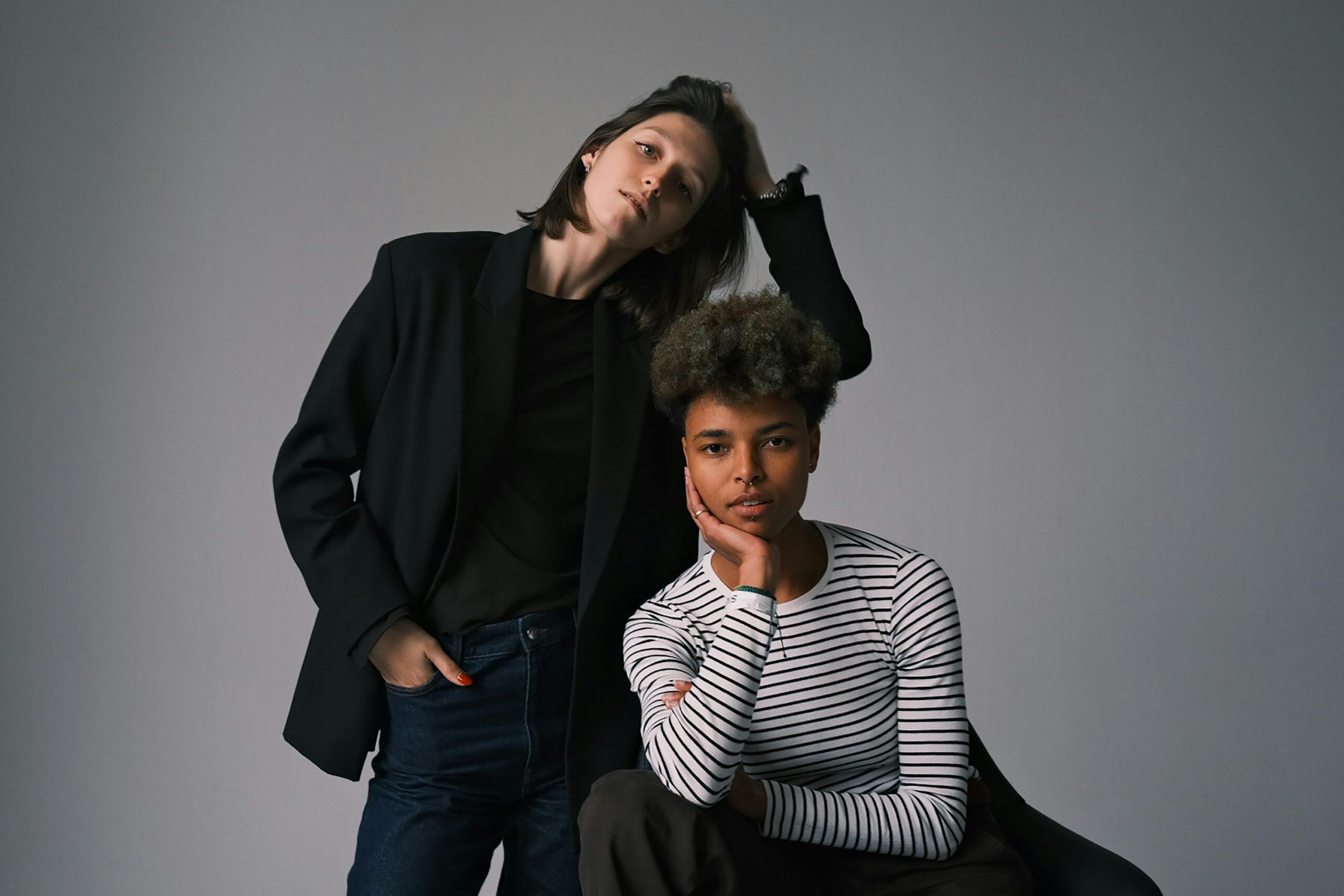A modern portrait of two stylish adults in casual and elegant attire posing indoors.