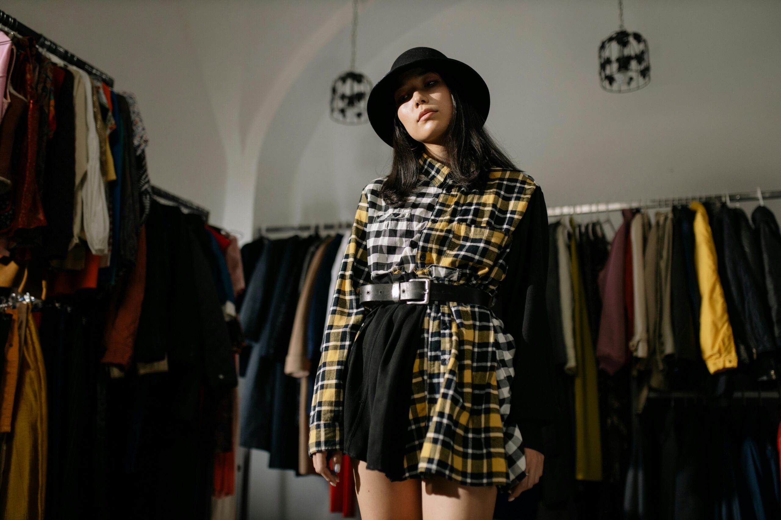 Stylish woman in a plaid outfit and hat posing in a vintage clothing store.